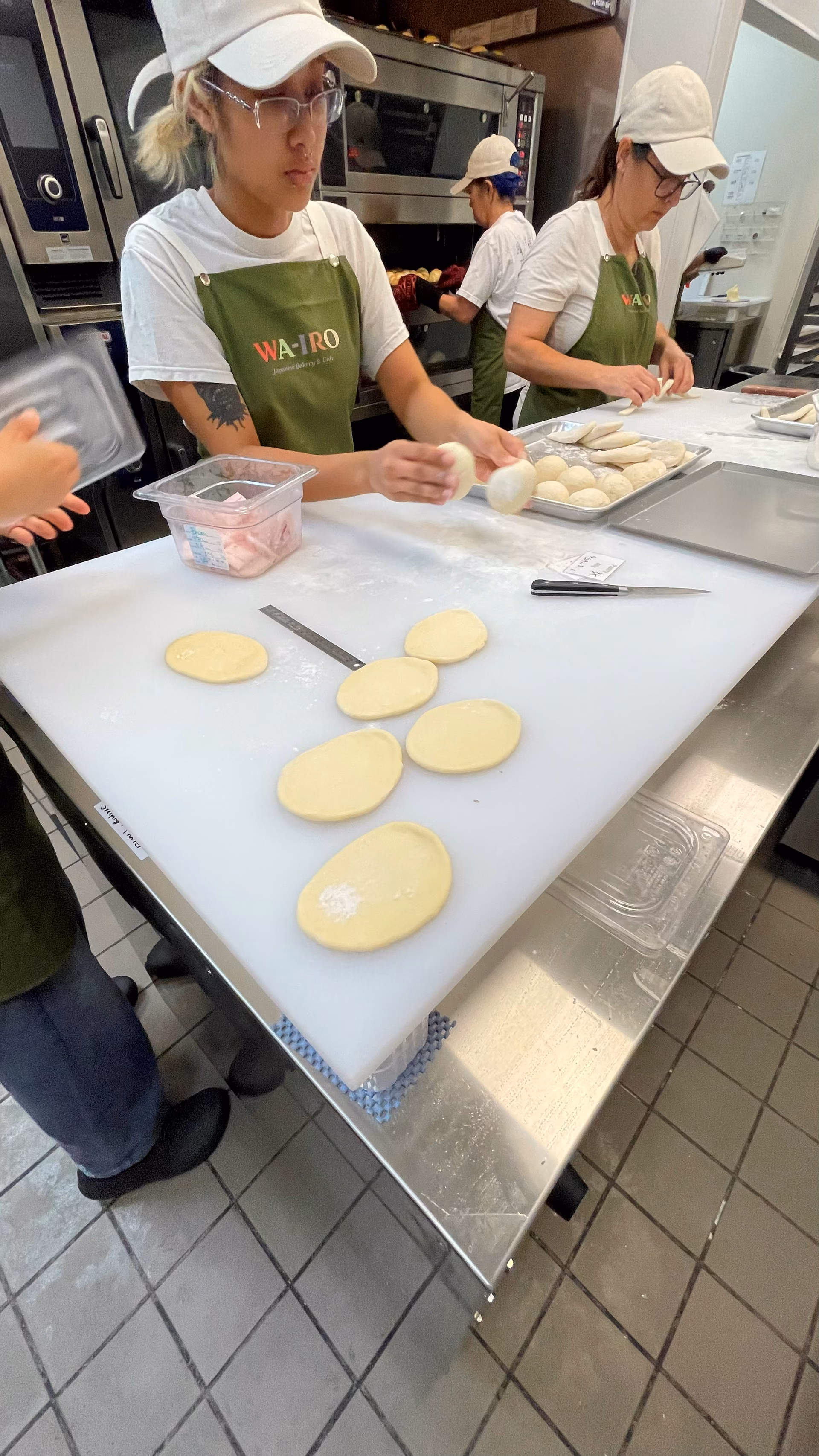 Close view of hands shaping small rounds of dough on a floured steel prep table.